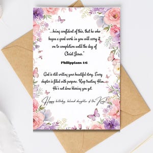 May include: A greeting card with a floral design in pink, purple, and white, featuring butterflies and text. The card is placed inside a brown envelope. The text includes a Bible verse and a birthday message.