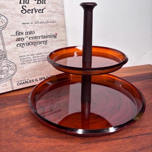 Peut inclure: Plateau de service à deux étages avec une base en bois brun et des étages en verre ambré. Le plateau est fabriqué par Charles G. Spilo Co. et est conçu pour s'intégrer à tout environnement de divertissement.