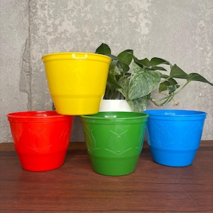 May include: A white ceramic mug with a black handle and the text "But First, Coffee" in a bold, black font. The mug is set against a blurred background. The mug is approximately 10 cm tall.