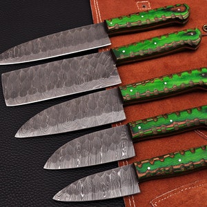 Könnte beinhalten: Ein Set aus sechs Küchenmessern mit gemusterten Stahlklingen und grün-braunen Holzgriffen. Die Messer sind auf einer braunen Lederrolle angeordnet. Die Klingen haben eine strukturierte Oberfläche.