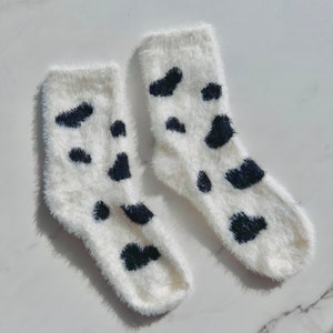 May include: A pair of white fuzzy socks with black cow print spots.