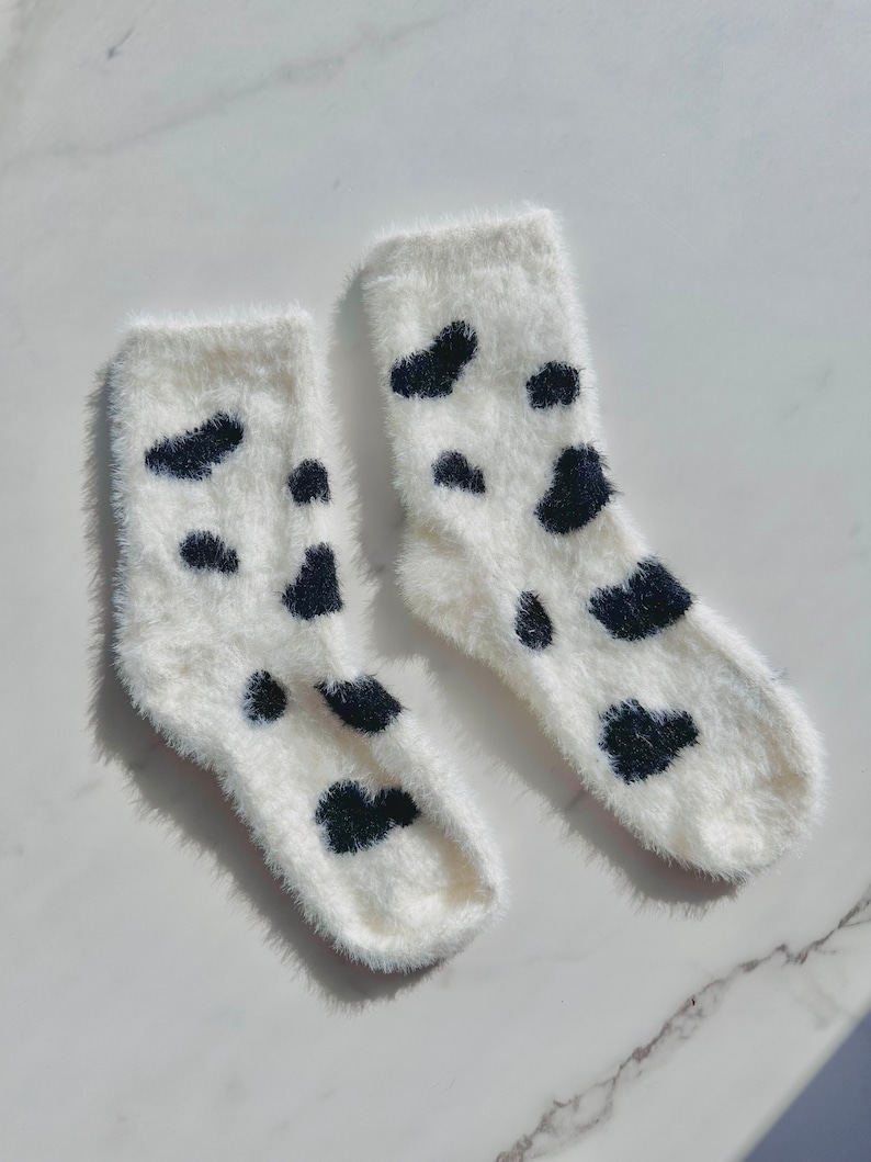 May include: A pair of white fuzzy socks with black cow print spots.
