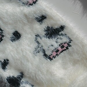 May include: White fuzzy sweater with a black and pink cow print design.