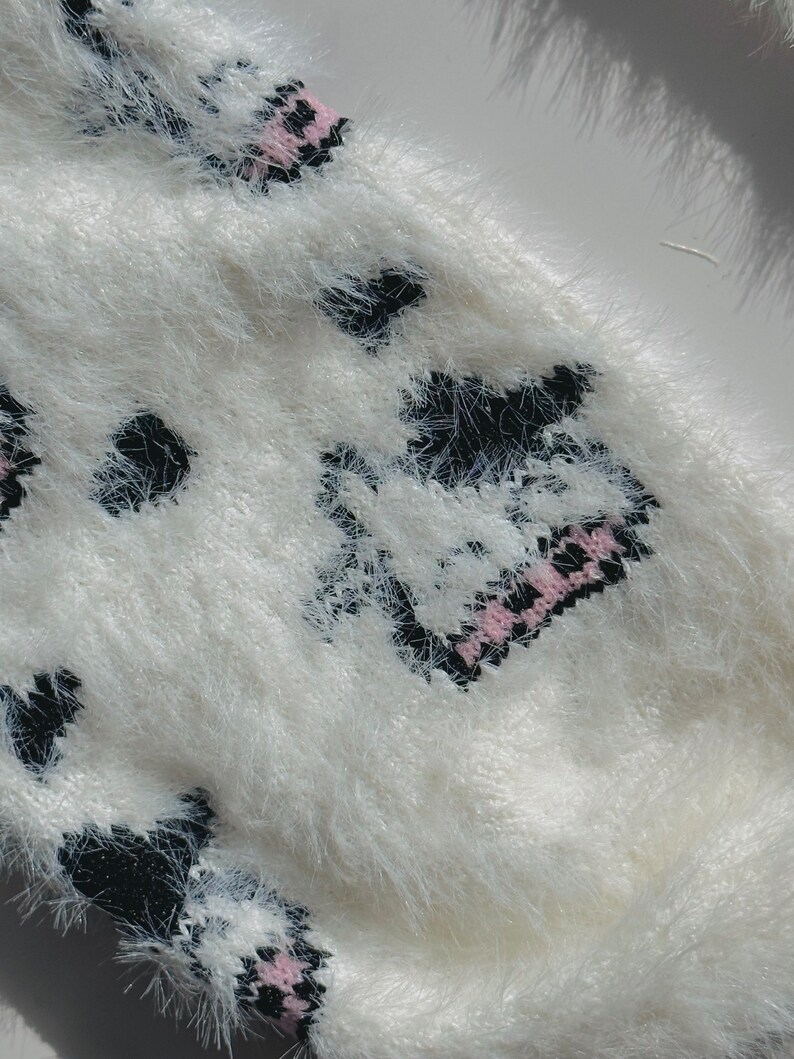 May include: White fuzzy sweater with a black and pink cow print design.