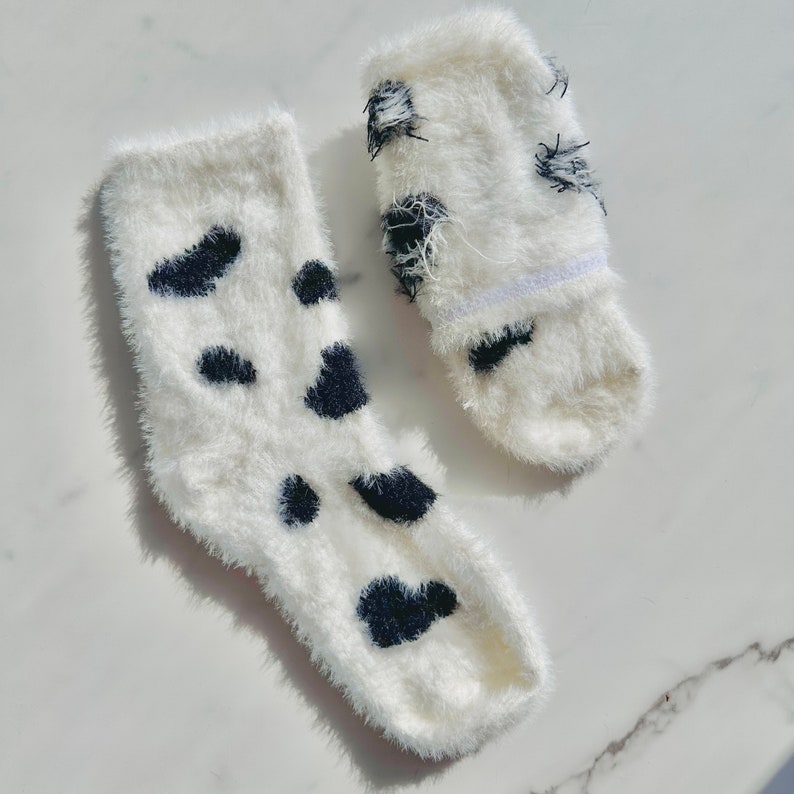 May include: A pair of white fuzzy socks with black spots. The socks are made of a soft, fluffy material and have a comfortable fit.