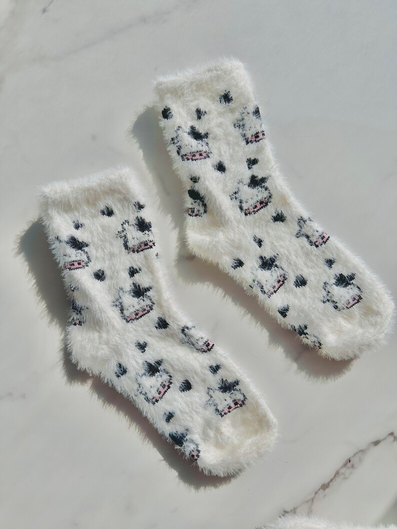 May include: A pair of white fuzzy socks with a black and pink cow print design.