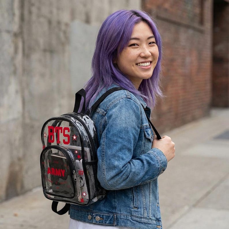 K&ouml;nnte beinhalten: Transparenter Rucksack mit dem roten Text "BTS". Der Rucksack hat einen schwarzen Griff und Tr&auml;ger sowie eine Seitentasche aus Netzstoff. Er ist mit roten Sternen und einem Camouflagemuster verziert.