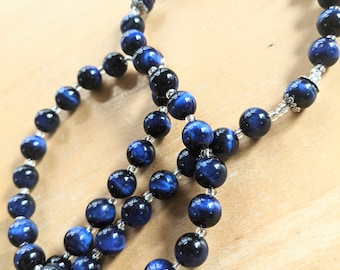 Può includere: Una collana di perline blu e nere con accenti argentati. Le perline sono rotonde e hanno una finitura liscia e lucida.