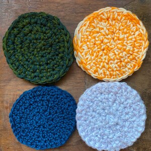 May include: Four crocheted coasters in different colors: green and brown, orange and white, blue, and light purple.