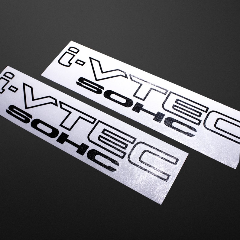 May include: Two rectangular white stickers with the text "i-VTEC SOHC" in black, stylized font. The stickers are angled, with a dark background. The text is bold and clear, suitable for automotive enthusiasts.
