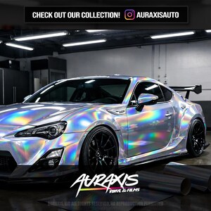 May include: A silver sports car with a holographic wrap, featuring black rims and a rear spoiler. The image includes the text "CHECK OUT OUR COLLECTION!" and the brand name "AURAXIS VINYL & FILMS".