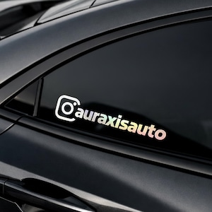 May include: A white and iridescent sticker with the Instagram logo and the text "@auraxisauto" is affixed to a car window. The sticker is visible against the dark background of the car's body and window.