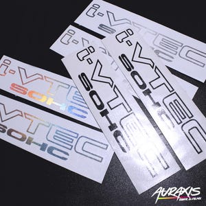 May include: Several white vinyl stickers with the text "i-VTEC SOHC" and "i-VTEC". The stickers have a metallic, holographic, and black finish. The brand name "AURAXIS VINYL & FILMS" is visible in the bottom right corner.