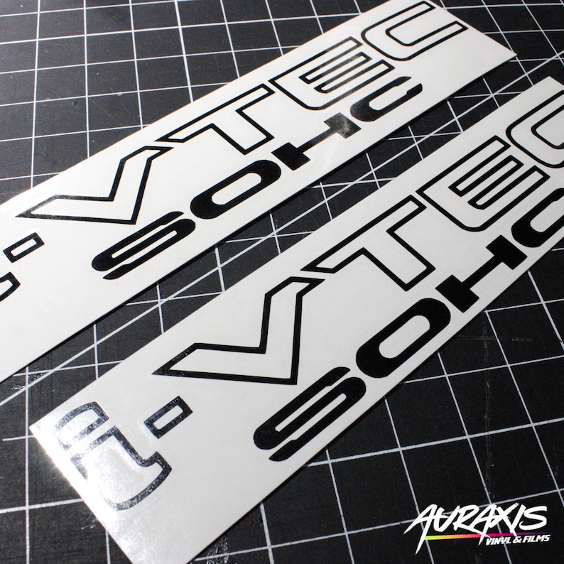 May include: Two white vinyl stickers with the text "VTEC SOHC" in black. The stickers are rectangular and have a glossy finish. The background is a black grid.