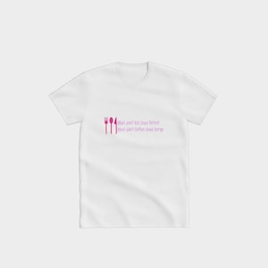Puede incluir: Camiseta blanca con un tenedor, una cuchara y un cuchillo rosas. El texto en la camiseta dice: "Lo que no mata engorda, Lo que no engorda purga."