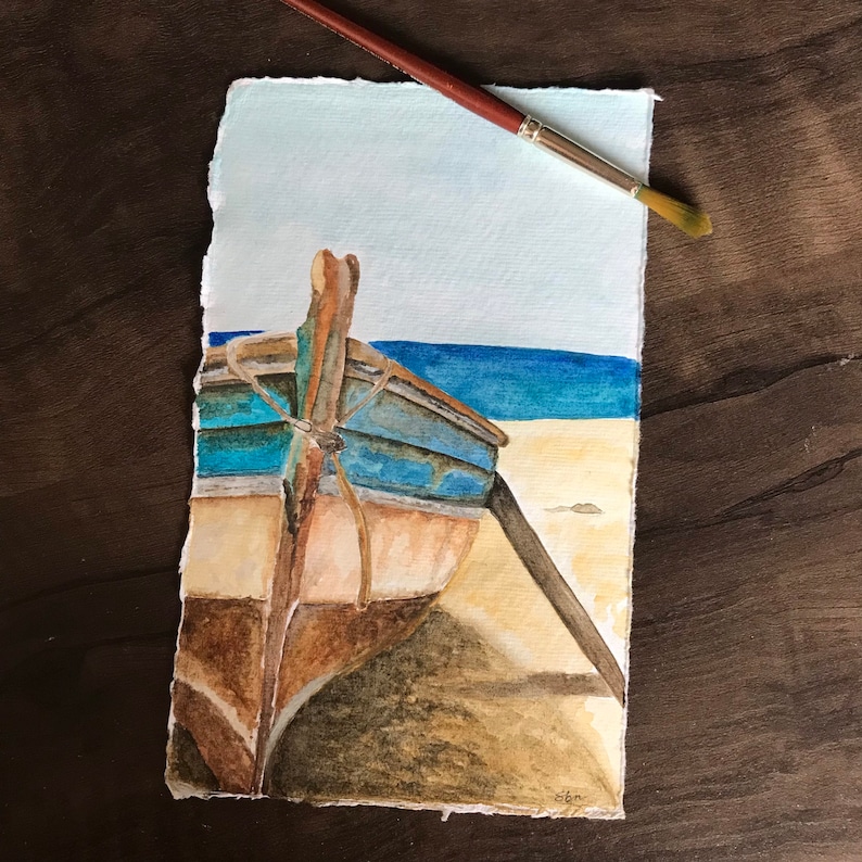 May include: Watercolor painting of a wooden boat on a sandy beach with blue water in the background. The boat is weathered and has a blue and brown paint job. The painting is signed "cbn" in the bottom right corner.