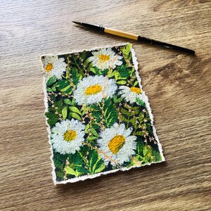 May include: A hand-painted watercolor illustration of a field of white daisies with yellow centers on a dark green background. The flowers are arranged in a random pattern and the edges of the paper are torn.