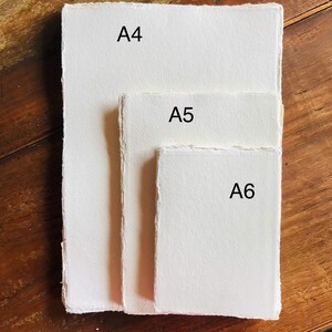 May include: Three sheets of white paper, labeled A4, A5, and A6, are stacked on a wooden surface. The sheets are all the same color and texture, but they are different sizes.