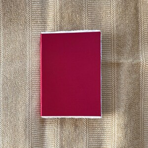 May include: A solid red square with white edges. The square is on a beige textured background.