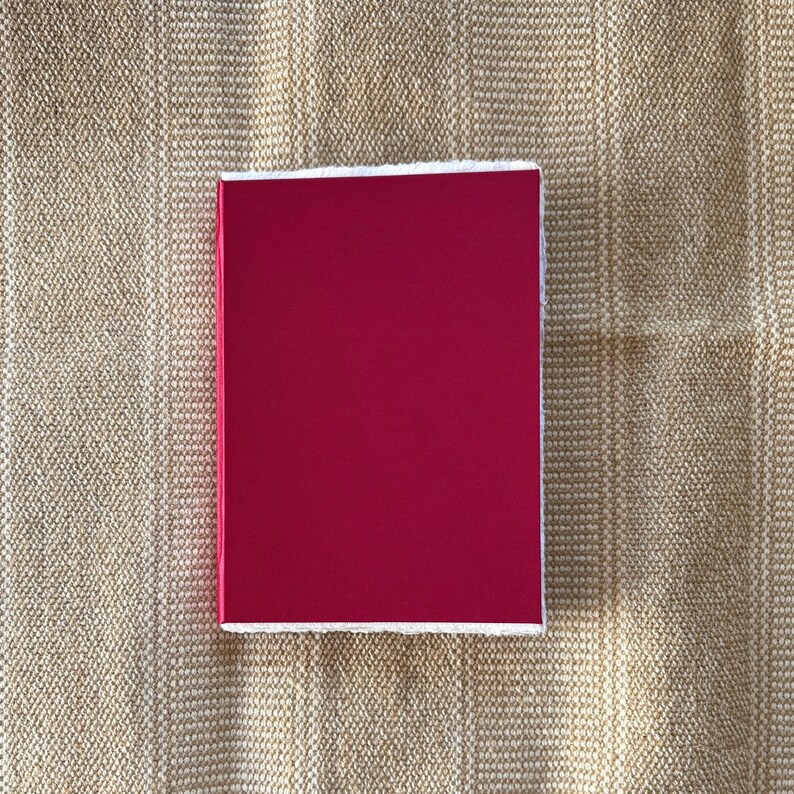 May include: A solid red square with white edges. The square is on a beige textured background.