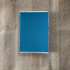 May include: A teal blue box with a white border. The box is sitting on a brown textured surface.