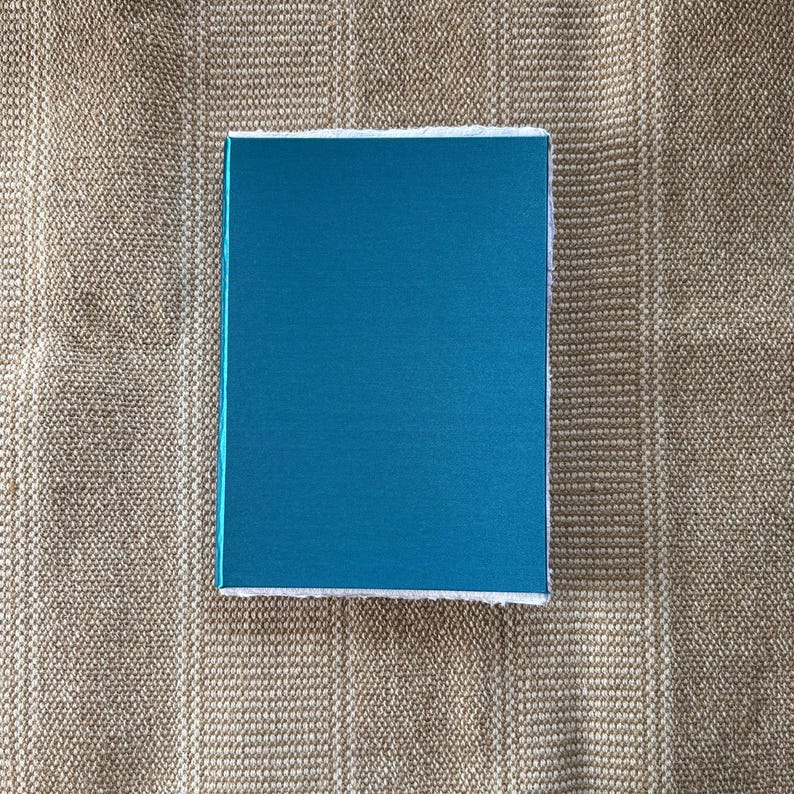 May include: A teal blue box with a white border. The box is sitting on a brown textured surface.