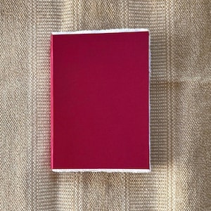 Op de afbeelding: Een rechthoekig, magentakleurig object met een witte rand. Het object staat tegen een getextureerde, beige achtergrond. De magentakleur is effen en levendig.