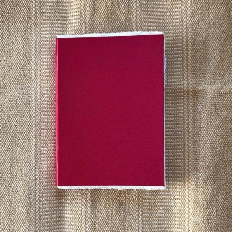Op de afbeelding: Een rechthoekig, magentakleurig object met een witte rand. Het object staat tegen een getextureerde, beige achtergrond. De magentakleur is effen en levendig.