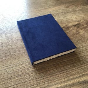 May include: A small, navy blue notebook with a white spine. The notebook is closed and lying on a wooden surface.