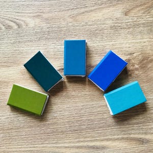 Pu&ograve; includere: Cinque piccole scatole rettangolari disposte a semicerchio. Le scatole sono dipinte in tonalit&agrave; di blu, verde e turchese.