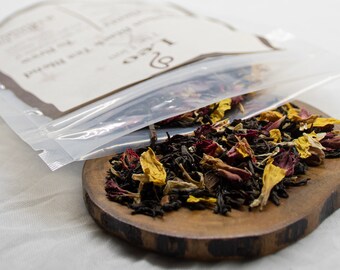 May include: A clear plastic bag labelled "Loose Leaf Tea" is open, spilling a blend of black tea, red and yellow flower petals onto a wooden surface.