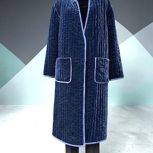 May include: A long, quilted navy blue coat with a subtle sheen. The coat features two front pockets and light blue trim along the edges and collar. The coat is displayed on a mannequin, paired with black pants.