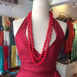 May include: A red halter dress with a red beaded necklace. The dress has a wrap style and a flowing skirt.