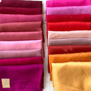 Könnte beinhalten: Eine Sammlung gefalteter Stoffe in verschiedenen Rot-, Rosa- und Goldtönen. Die Stoffe sind ordentlich gestapelt und zeigen eine Reihe von Farben von tiefem Burgunder bis hin zu hellem Fuchsia und Goldgelb. Ein kleines Etikett mit der Nummer 120 ist sichtbar.