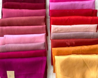 May include: A collection of folded fabric in various shades of red, pink, and gold. The fabrics are neatly stacked, showcasing a range of colors from deep burgundy to bright fuchsia and golden yellow. A small tag with the number 120 is visible.