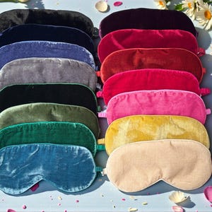 Puede incluir: Una variedad de antifaces de terciopelo en varios colores, incluyendo negro, azul marino, azul, gris, negro, verde, turquesa, burdeos, rojo, rosa, amarillo y beige. Cada antifaz tiene una banda elástica. Margaritas y pétalos esparcidos.