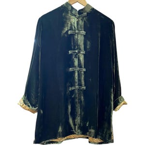 Peut inclure: Veste en velours vert foncé avec un col mandarin et des fermetures à brandebourgs. La veste à manches longues a une garniture dorée aux poignets et à l'ourlet. La veste est suspendue à un cintre en bois.