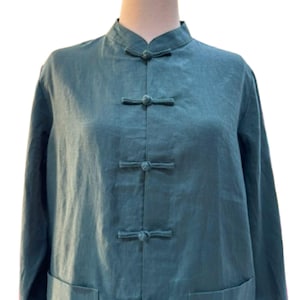Könnte beinhalten: Ein langärmliges Hemd in Tealblau mit einem Mandarin-Kragen und fünf dekorativen Knöpfen. Das Hemd hat zwei Taschen unten.
