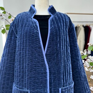May include: A quilted navy blue jacket with a light blue trim. The jacket has a stand-up collar, two front pockets, and a vertical stitched pattern. The jacket is displayed on a mannequin.