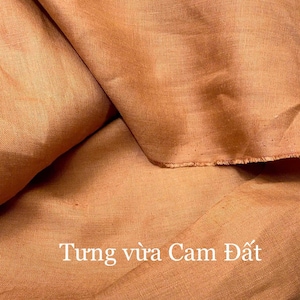 Puede incluir: Primer plano de una tela naranja doblada. La tela tiene un aspecto texturizado y un borde sin rematar. El texto "Tung vừa Cam Đất" est&aacute; impreso en blanco en la parte inferior de la imagen.