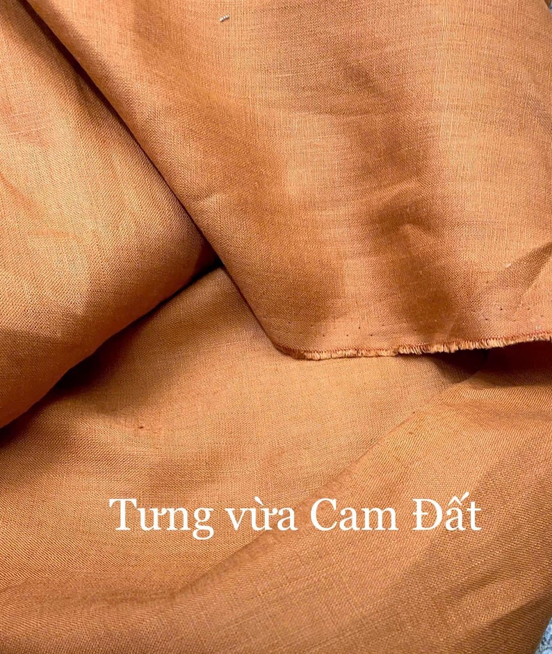 Puede incluir: Primer plano de una tela naranja doblada. La tela tiene un aspecto texturizado y un borde sin rematar. El texto "Tung vừa Cam Đất" est&aacute; impreso en blanco en la parte inferior de la imagen.