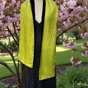 May include: A long, rectangular scarf featuring a vibrant chartreuse, crinkled fabric on the outer panels and a solid black velvet trim along the inner edges. The scarf is draped over a mannequin wearing a black lace dress.