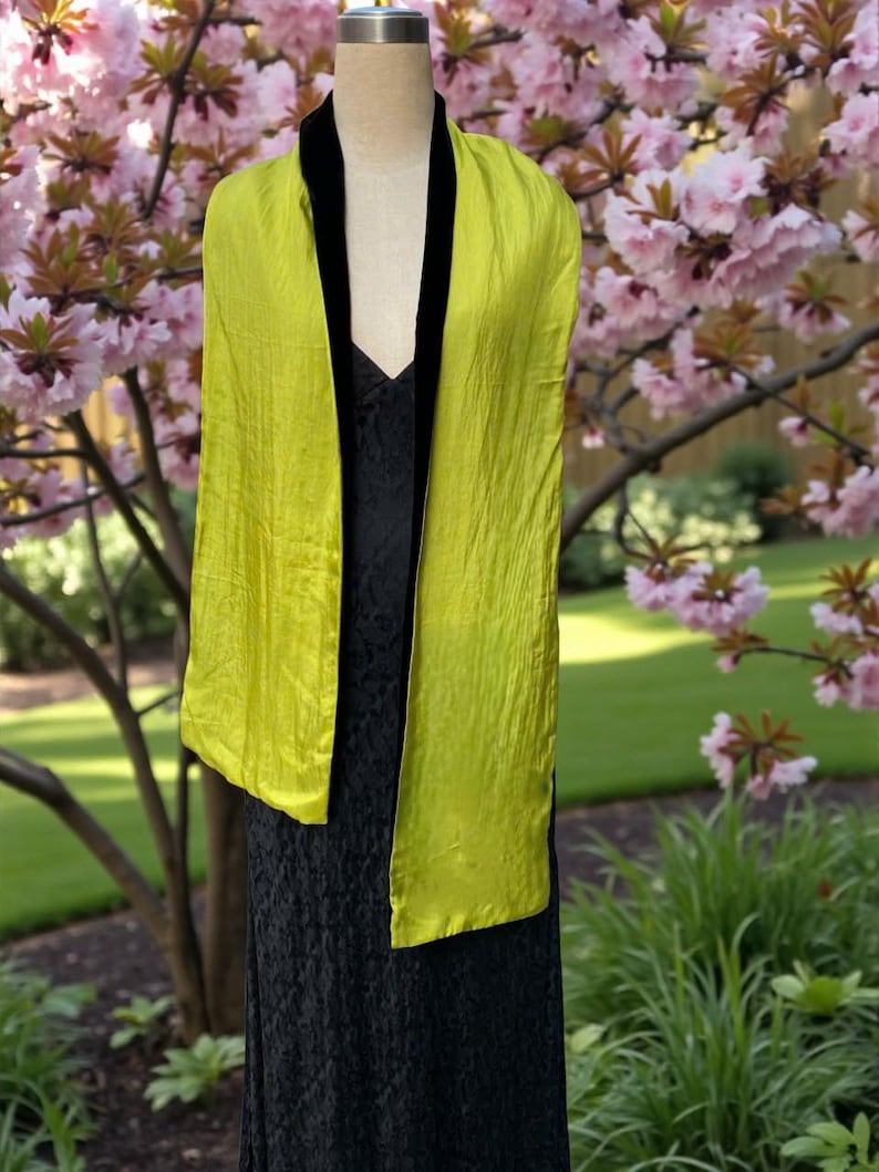 May include: A long, rectangular scarf featuring a vibrant chartreuse, crinkled fabric on the outer panels and a solid black velvet trim along the inner edges. The scarf is draped over a mannequin wearing a black lace dress.