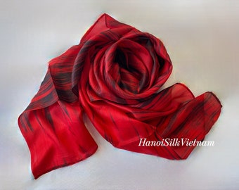 May include: Red silk scarf with black abstract brushstrokes. The scarf is folded into a rose shape. The text "HanoiSilk Vietnam" is visible in the lower right corner.