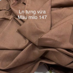 May include: Close-up of a folded fabric in a warm, brown colour. The fabric has a textured appearance and is draped in soft folds. Text in white reads "Ln tung vừa M&agrave;u milo 147".