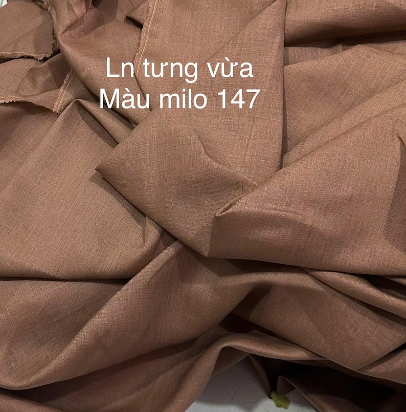 May include: Close-up of a folded fabric in a warm, brown colour. The fabric has a textured appearance and is draped in soft folds. Text in white reads "Ln tung vừa M&agrave;u milo 147".