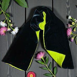 May include: A long, rectangular scarf featuring a deep black velvet exterior and a vibrant lime green velvet interior. The scarf is draped in a folded position, showcasing the contrasting colors of the two fabric sides in a smooth texture.