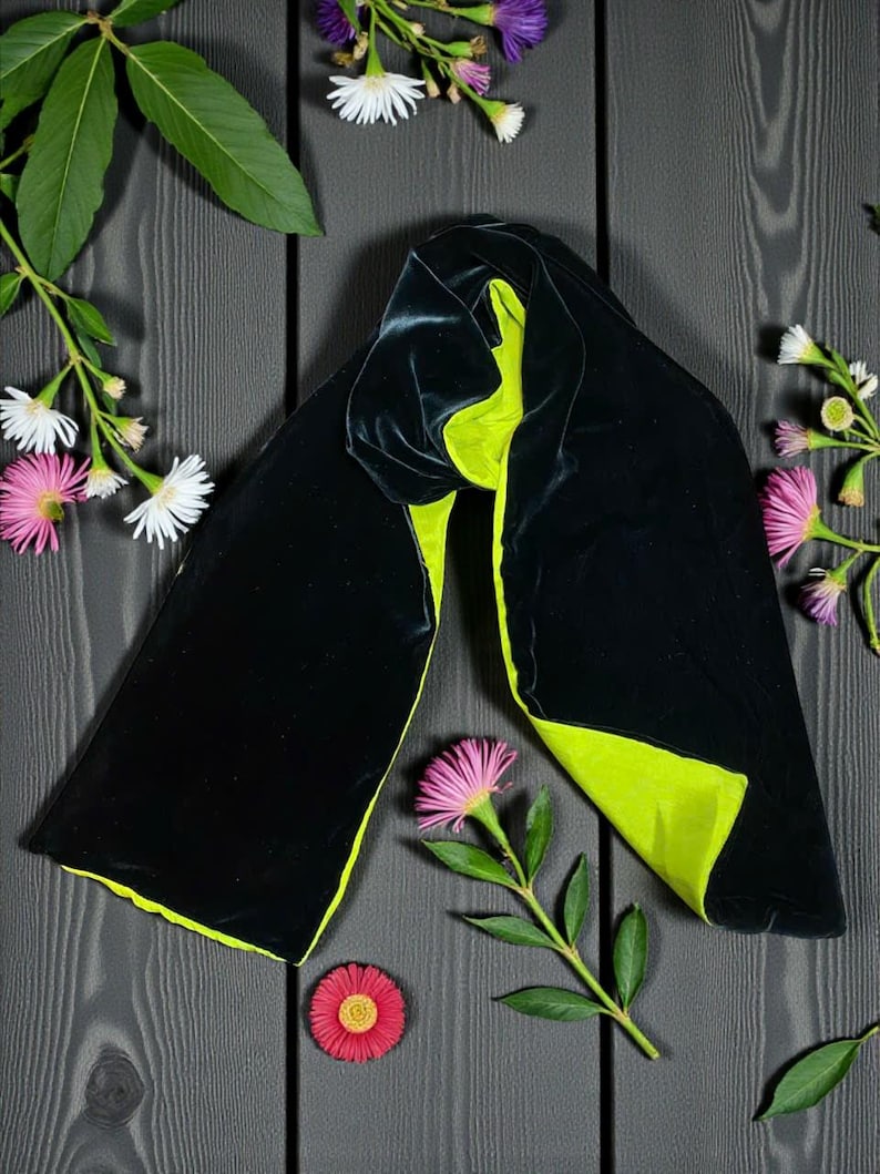 May include: A long, rectangular scarf featuring a deep black velvet exterior and a vibrant lime green velvet interior. The scarf is draped in a folded position, showcasing the contrasting colors of the two fabric sides in a smooth texture.