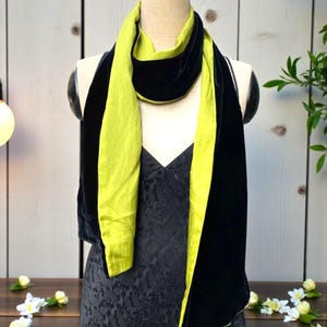 May include: A long, reversible scarf featuring a vibrant lime green side and a deep black velvet side. The scarf is draped around the neck of a mannequin, showcasing the contrasting textures and colors of the fabric as it hangs down the front.