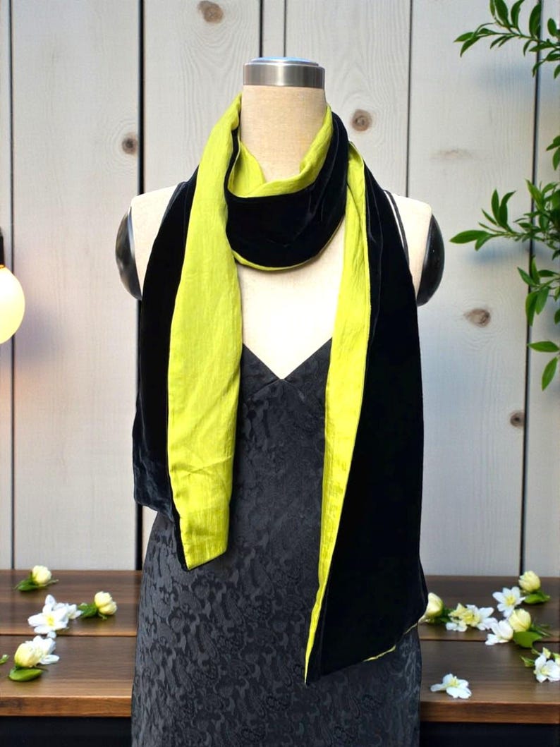 May include: A long, reversible scarf featuring a vibrant lime green side and a deep black velvet side. The scarf is draped around the neck of a mannequin, showcasing the contrasting textures and colors of the fabric as it hangs down the front.